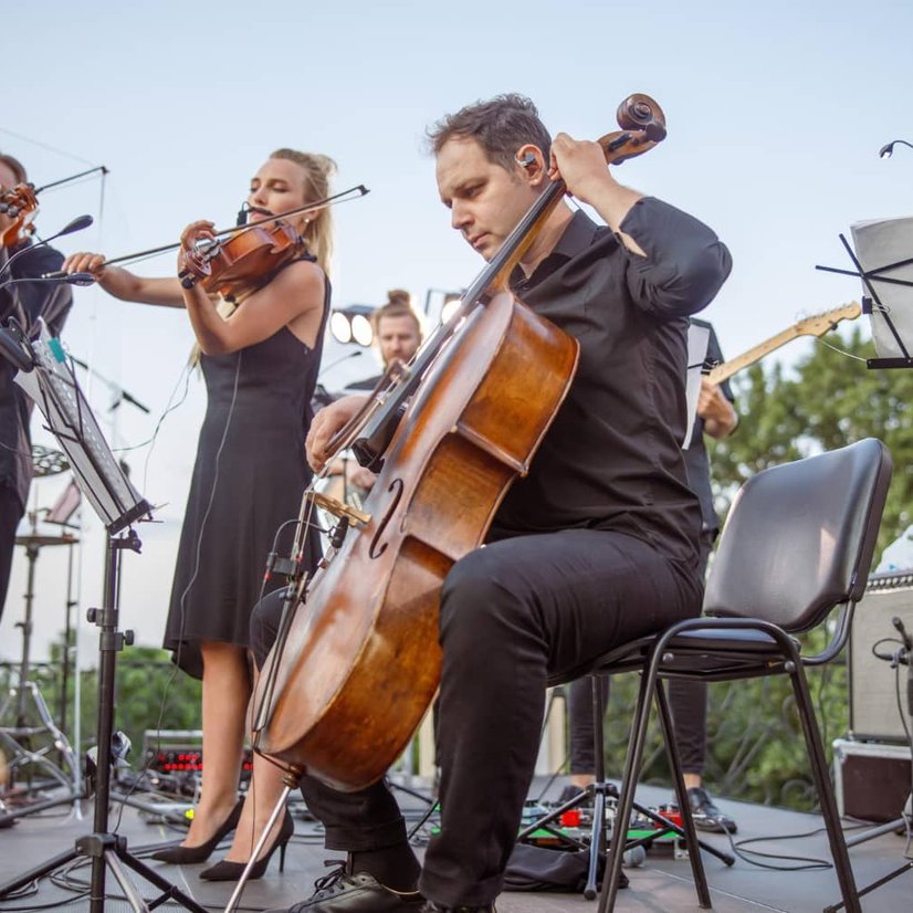 Orchestra performing outdoors with cello and violin musicians on stage