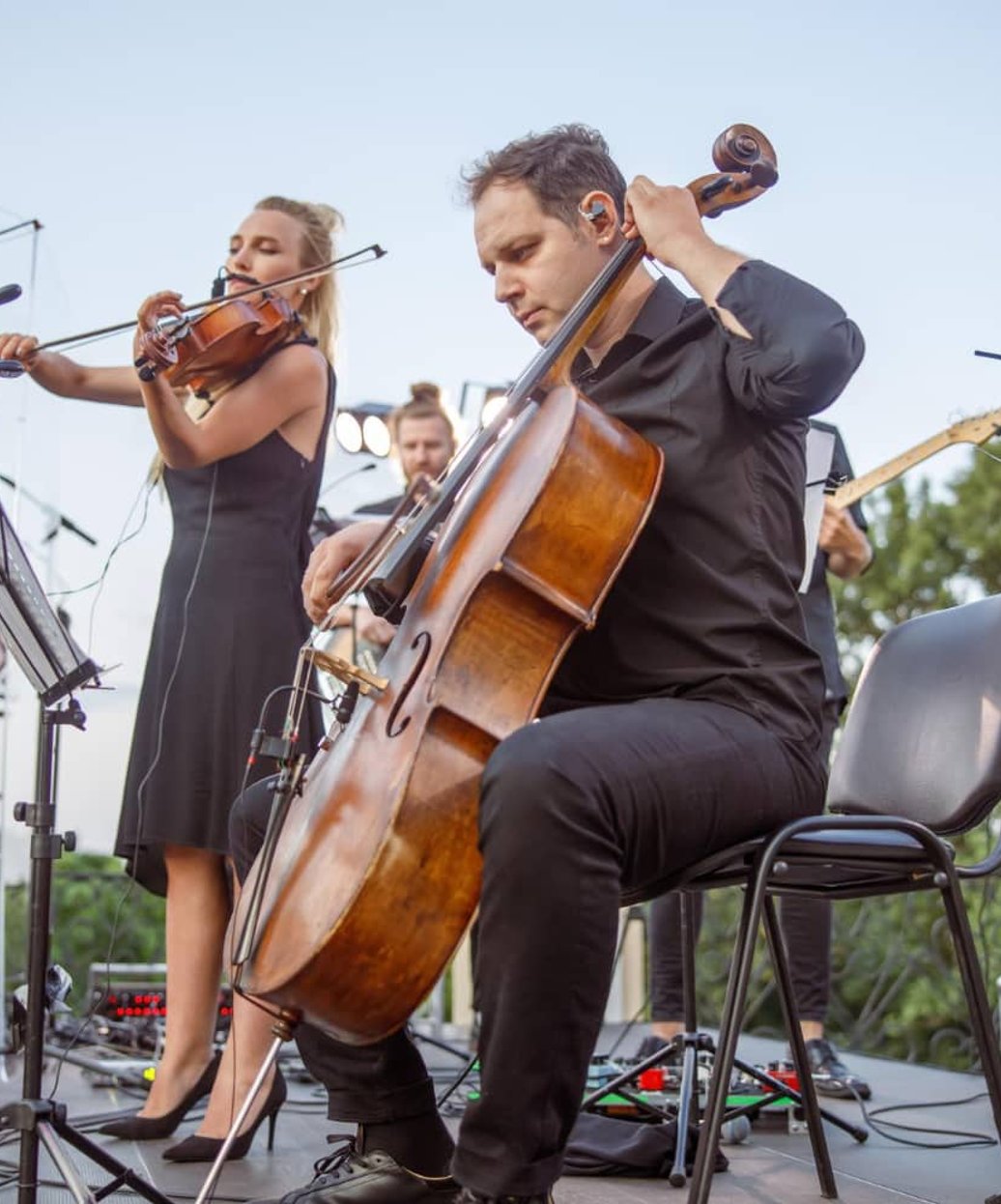Orchestra performing outdoors with cello and violin musicians on stage