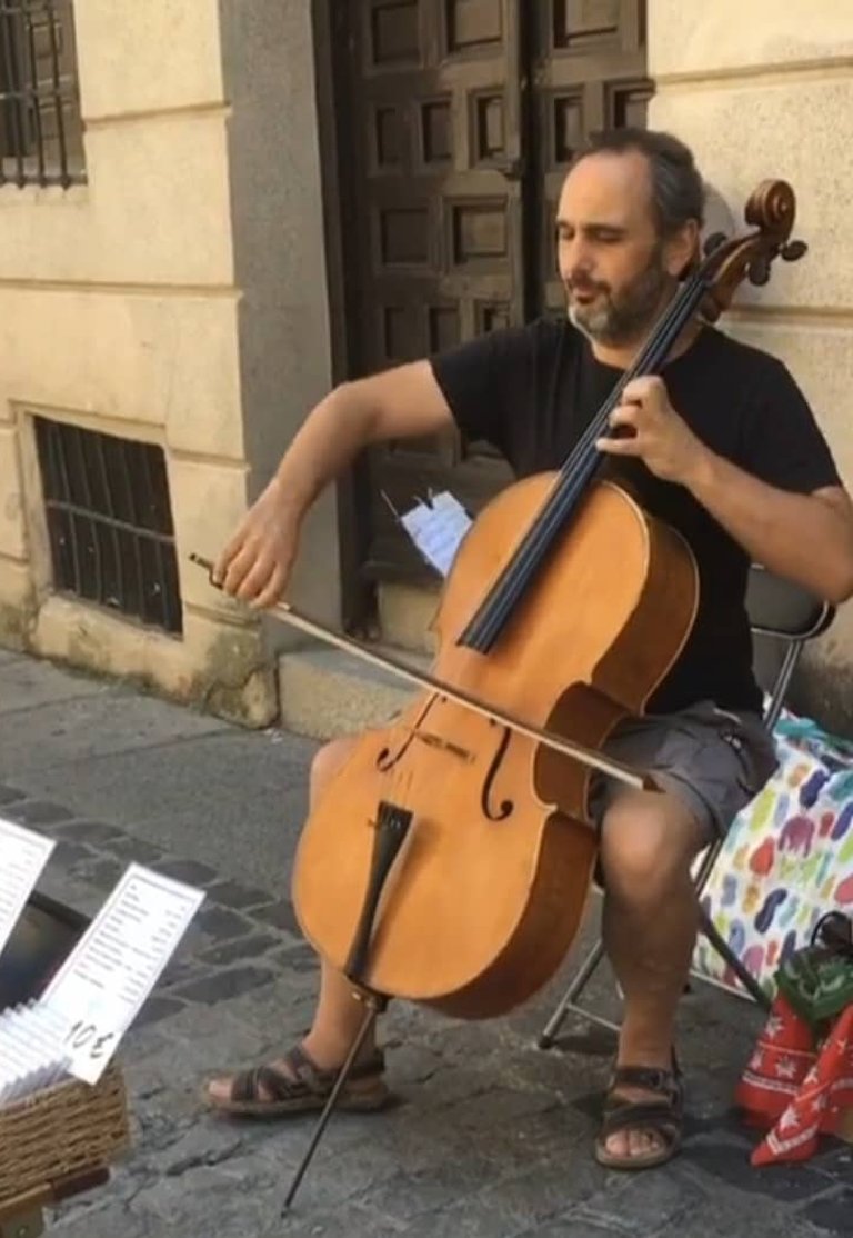 Street performer playing cello outdoors with sheet music displayed