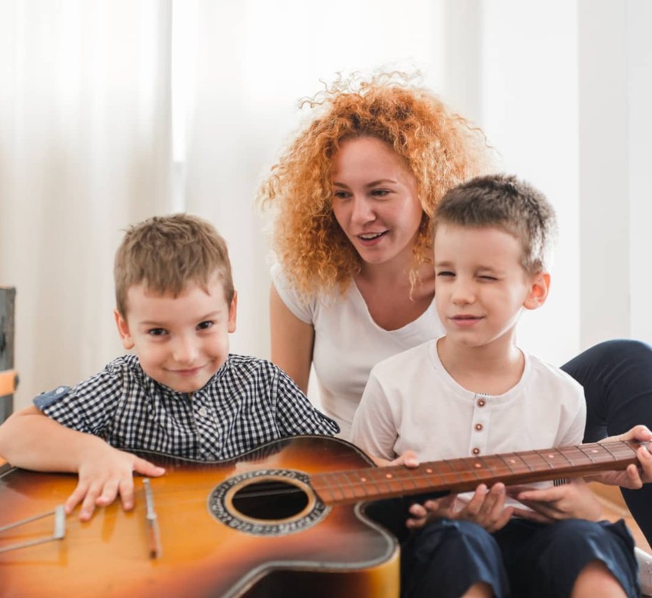 Woman with two boys holding acoustic guitar together