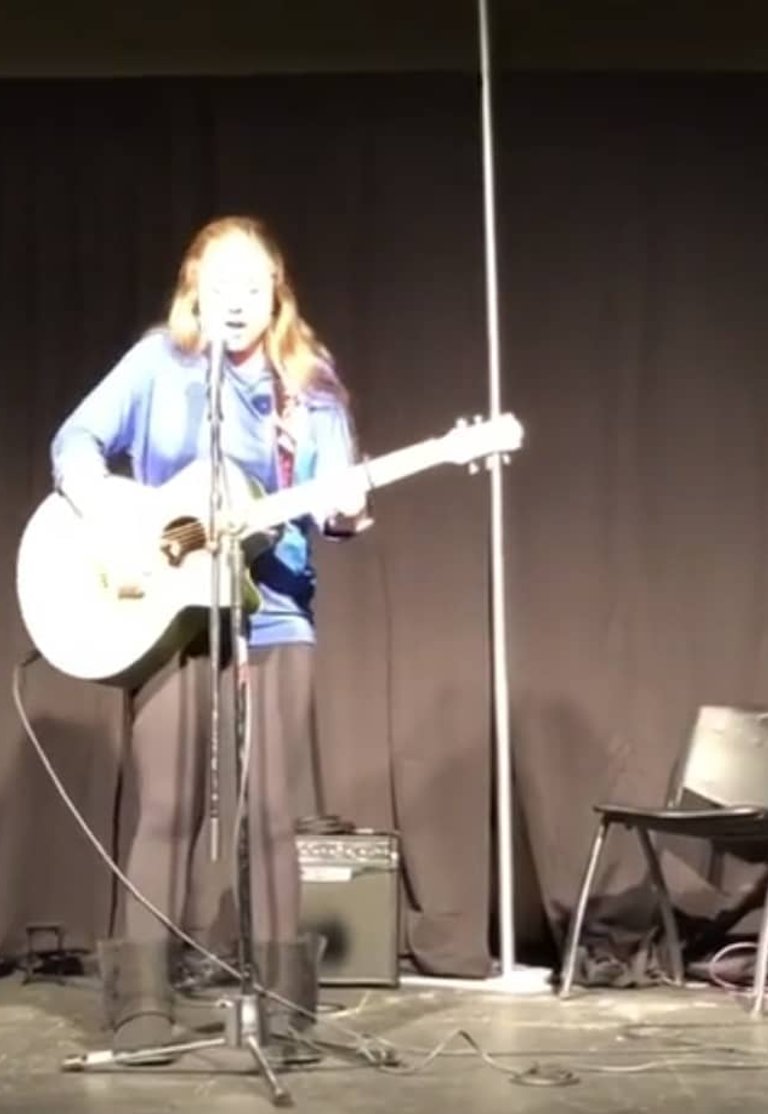 Young performer with white guitar on stage at microphone