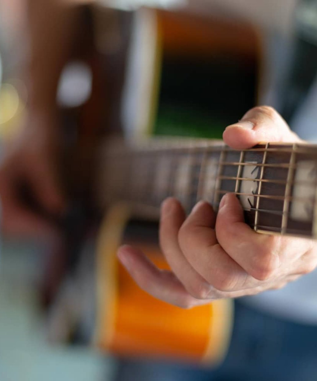 Close-up of hands playing chords on acoustic guitar fretboard