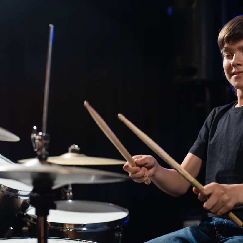 Smiling boy playing drum set with drumsticks in studio