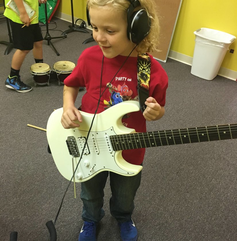 Young girl wearing headphones holding white electric guitar during music lesson