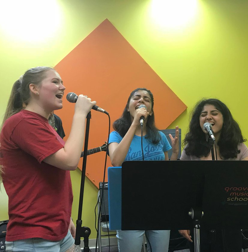 Three teenage girls singing into microphones together during group vocal lesson