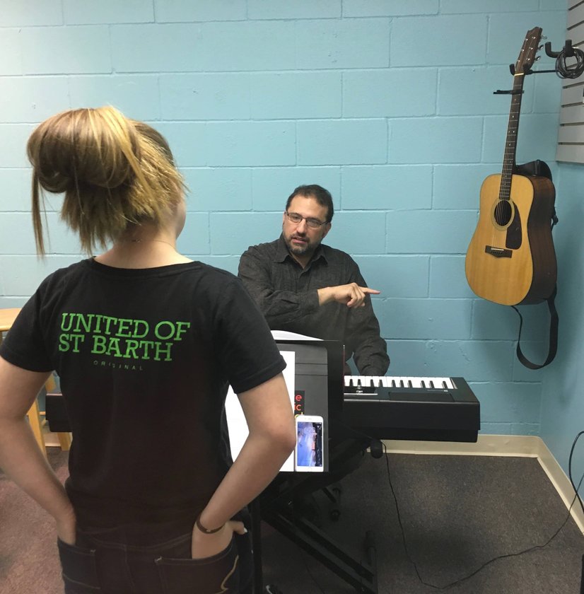 Music instructor teaching student keyboard lesson with tablet in blue practice room
