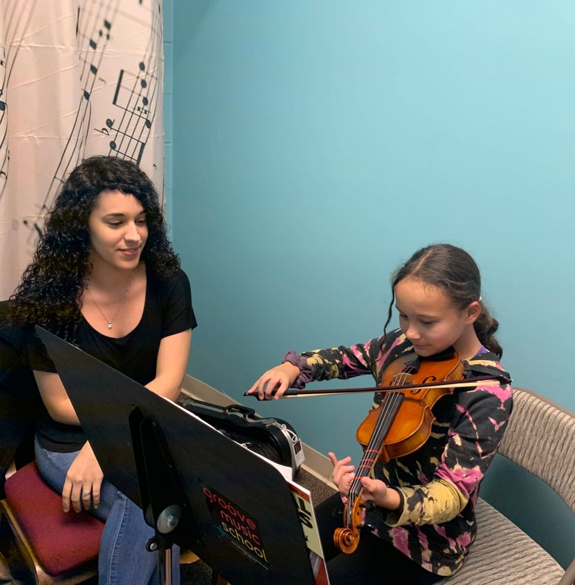 Violin teacher guiding young girl during private lesson with sheet music stand
