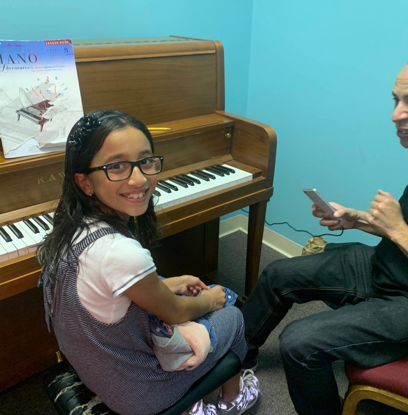 Smiling girl at piano bench during lesson with instructor in blue room