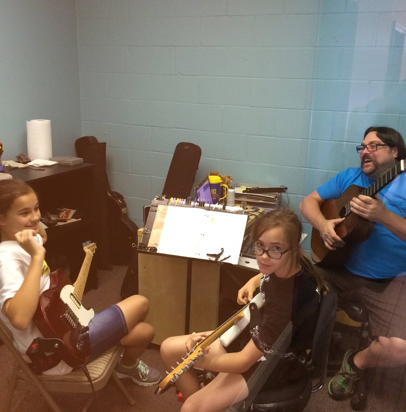 Teacher playing guitar with two young students learning instruments in lesson room