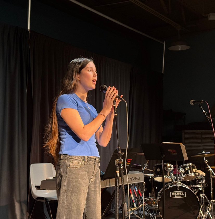 Teen girl singing into microphone on stage with drum set behind her