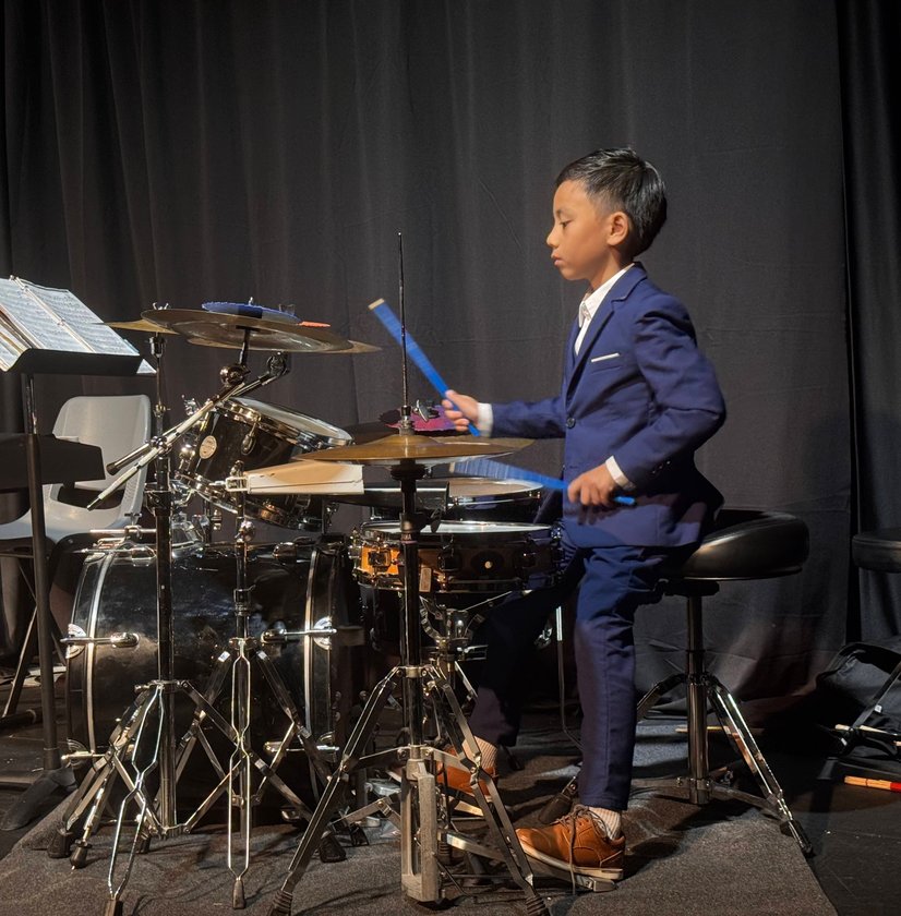 Young boy in navy suit playing drum set during recital performance onstage