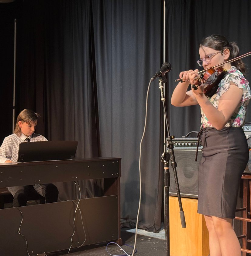 Girl playing violin on stage while another student accompanies on piano below