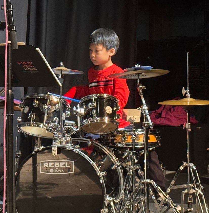 Young boy in red shirt performing on drum set during stage recital