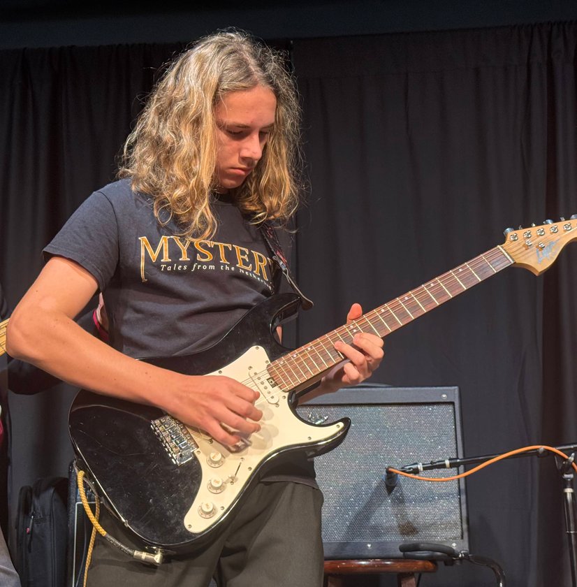 Teen playing electric guitar on stage during band performance with black curtain