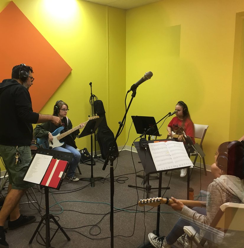 Instructor teaching band class with students playing guitar and bass in studio