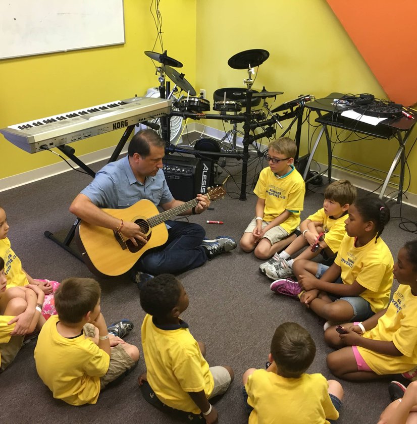 Teacher with acoustic guitar leading group of young children in yellow shirts